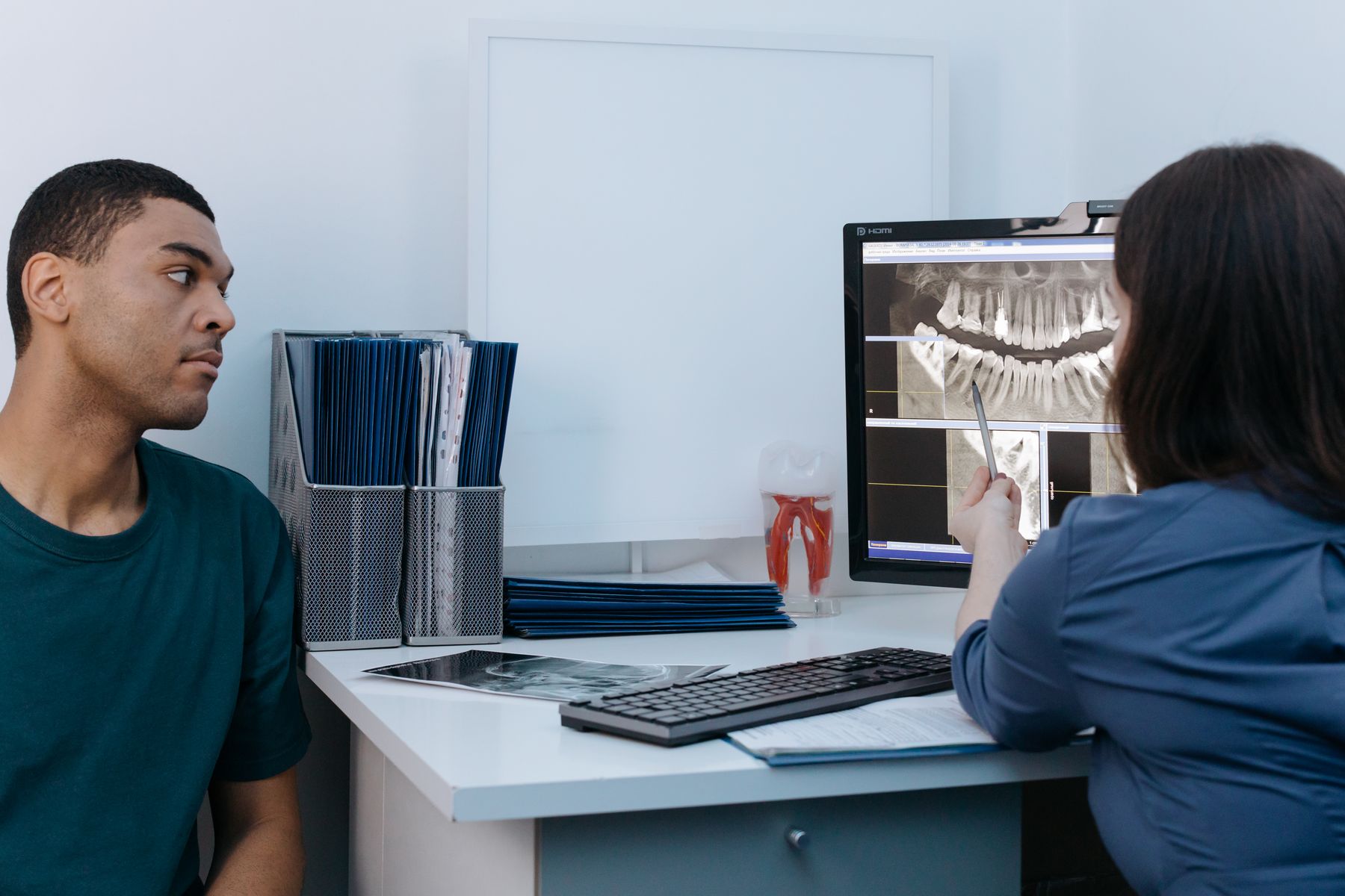 A patient in a green T-shirt discussing dental X-rays with a clinician in a dental office.
