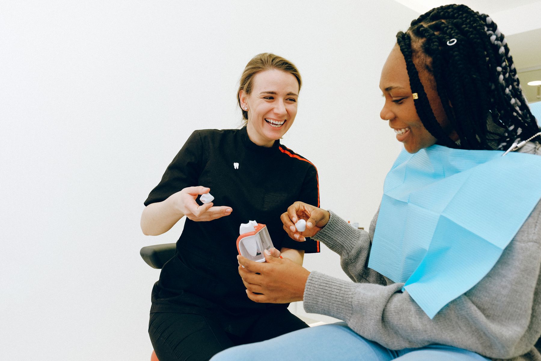 A dental professional and a smiling patient discuss a tooth model.