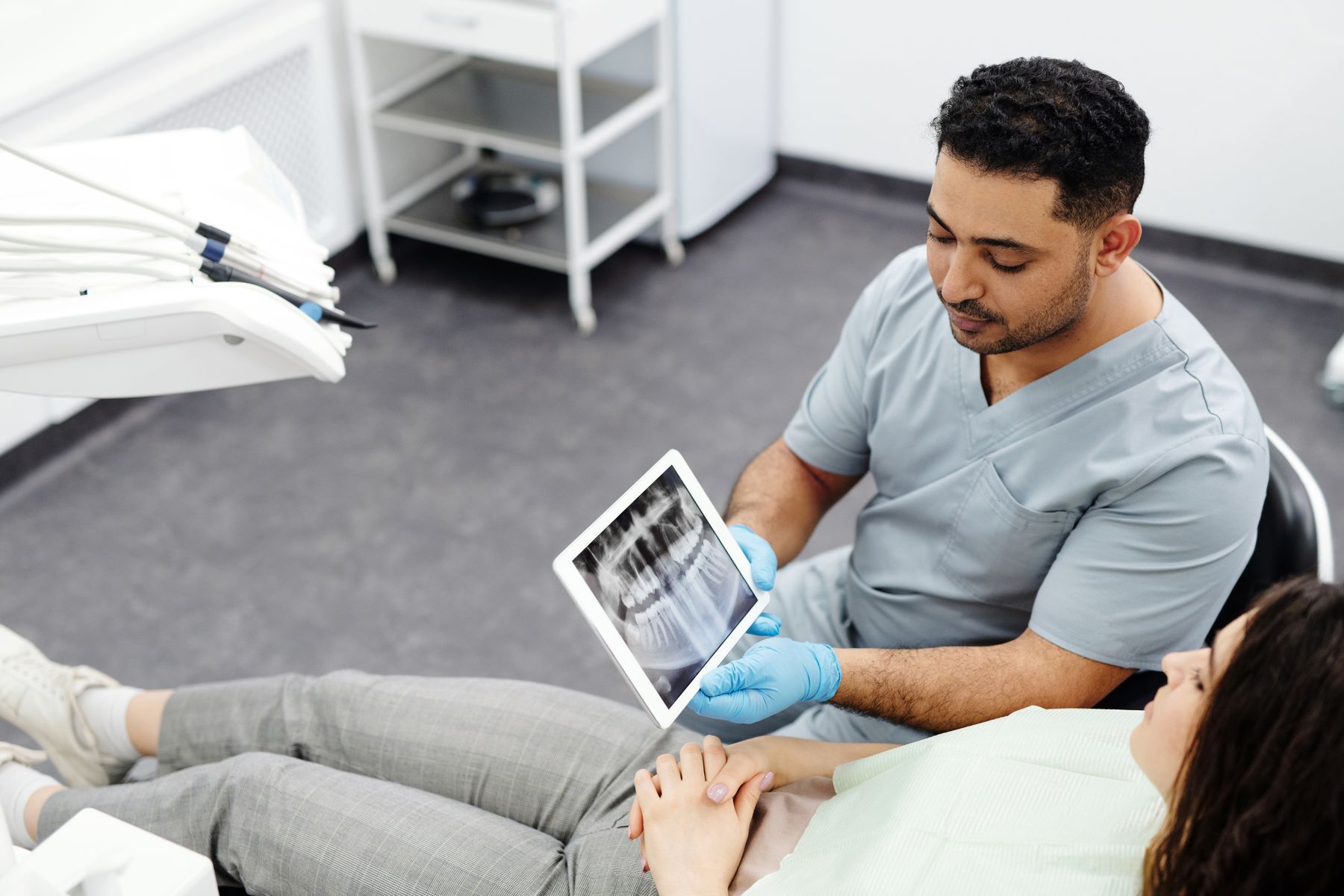 A male dentist reviewing a dental X-ray on a tablet with a patient seated in a dental chair.